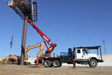 Flatbed truck-mounted Elliott Equipment aerial work platform with crew working on a billboard sign.