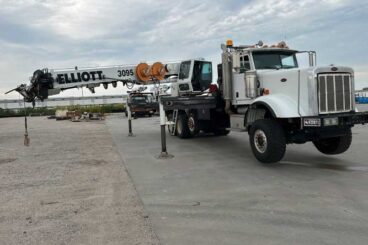 White utility digger derrick on boom truck platform parked outdoors on concrete surface.