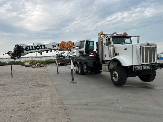 White utility digger derrick on boom truck platform parked outdoors on concrete surface.