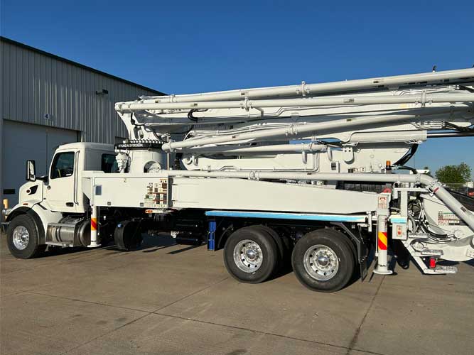 White concrete boom pump with dual rear axles parked outside industrial shop garage door