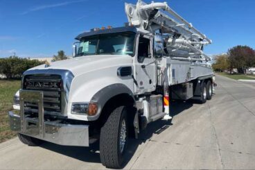 Heavy-duty industrial concrete pump boom truck with MACK on cab front grill parked outdoors under a blue sky.