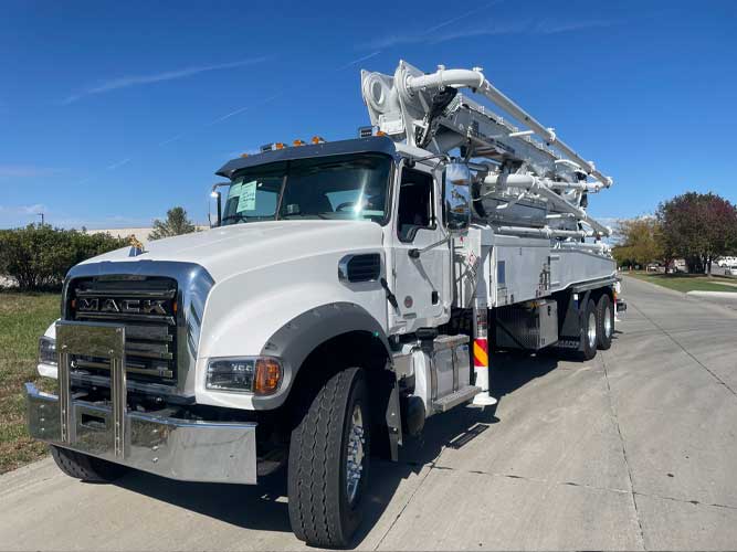 Heavy-duty industrial concrete pump boom truck with MACK on cab front grill parked outdoors under a blue sky.