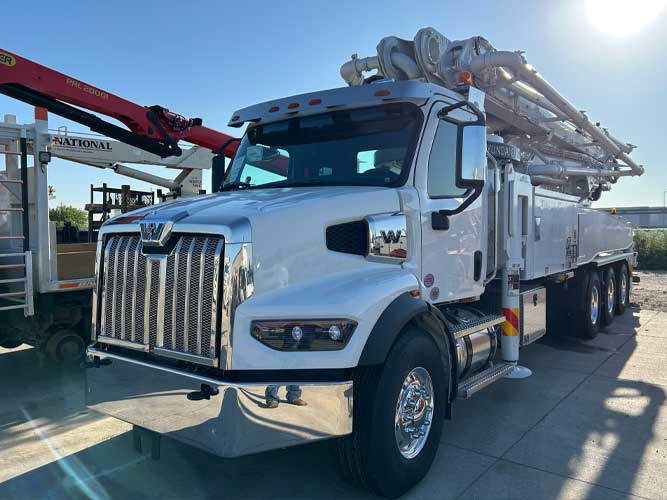 Concrete boom pump truck equipment parked on ashpalt. Front shows a Western Star cab.