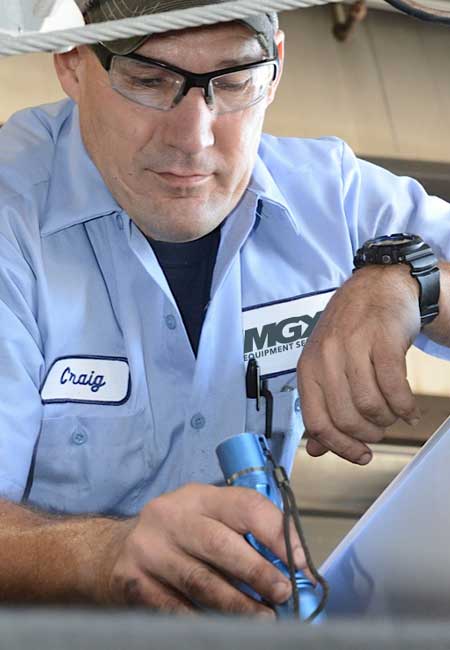 Mechanic technician wearing safety glass holding flashlight inspecting a machine for repair.
