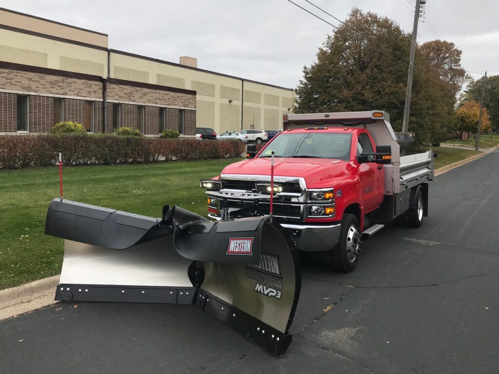 Front mounted Western MVP3 adjustable v-plow with dump body parked next to a curb outside an office building.