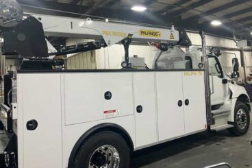 White mechanics truck with Palfinger branded service crane. Picture is inside a truck shop.