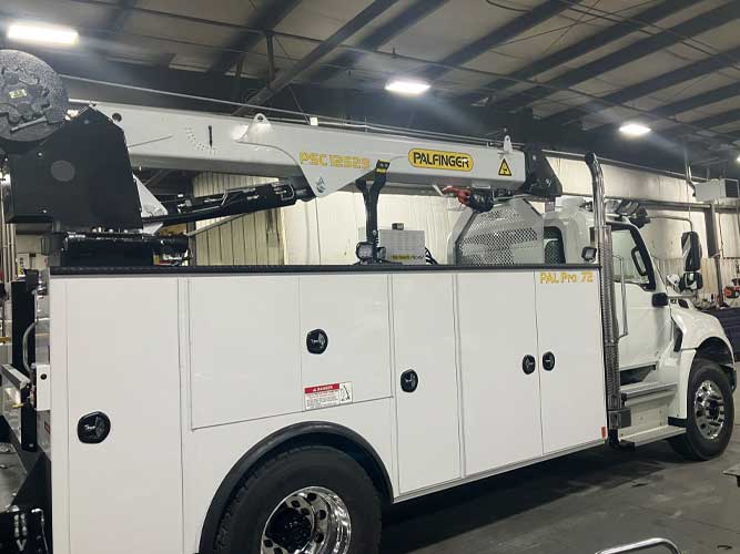 White mechanics truck with Palfinger branded service crane. Picture is inside a truck shop.