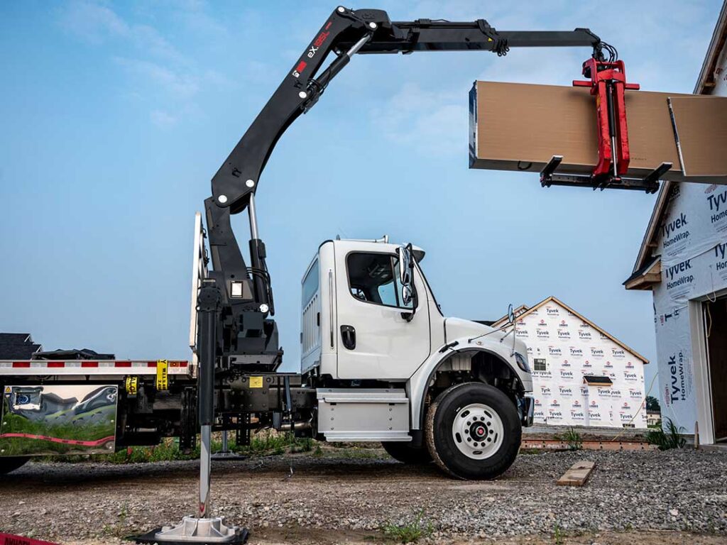 Flatbed work truck with HIAB heavy-duty knuckle boom crane parked in the driveway with extended boom over the roof of a home.