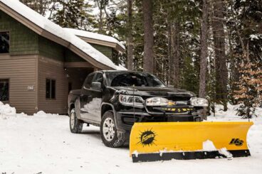 FISHER straight blade snow plow mounted on a pickup truck parked outdoors in front of a residential home.