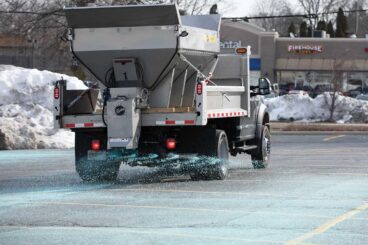 Truck with stainless steel hopper distributing material in a parking lot.