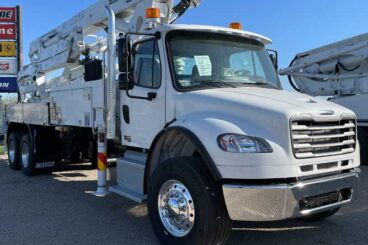 White concrete boom pump truck on Freightliner cab with folded boom, chrome bumper and wheel rims.