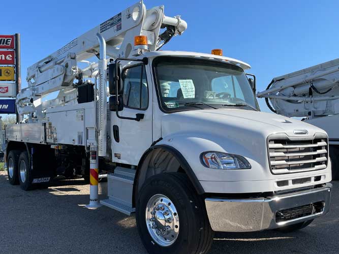 White concrete boom pump truck on Freightliner cab with folded boom, chrome bumper and wheel rims.