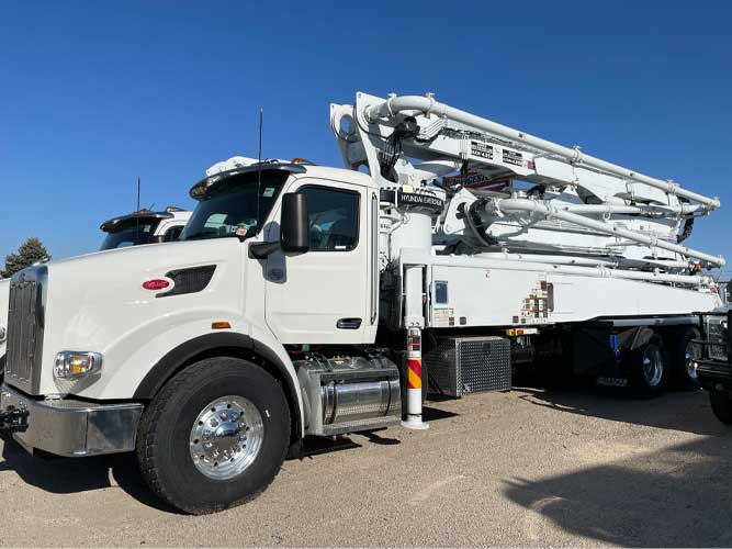 White concrete boom pump truck on Peterbilt cab tandem axle chassis