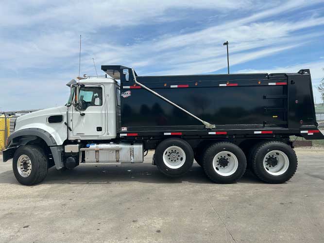 MAXX brand dump body mounted on white heavy-duty Mack standard cab chassis parked on a paved lot. Features tandem rear axles with pusher.