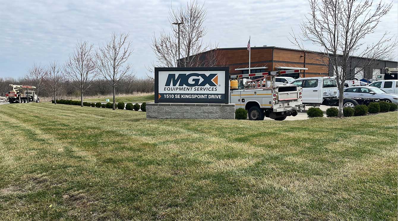 Sign for MGX Equipment Services 1510 SE Kingspoint Drive in Kansas City, Missouri, with several industry work trucks parked nearby.