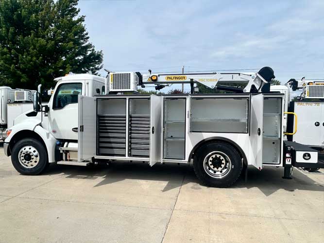 Large white work truck with mechanics body parked outdoors on concrete. Compartment doors opened showing shelves and drawers. Compressor and service crane labeled with Palfinger logo and PSC 10829 mounted on truck body.