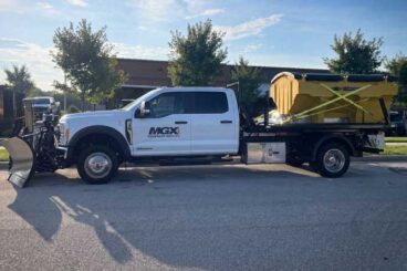 Commercial work truck crew cab chassis with stainless steel front plow and yellow spreader on flatbed