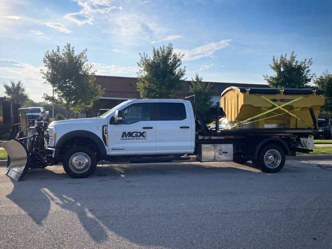 Commercial work truck crew cab chassis with stainless steel front plow and yellow spreader on flatbed