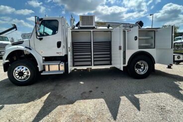 White commercial work truck with open truck body doors showing storage drawers, parked outdoors under partly sunny skies.