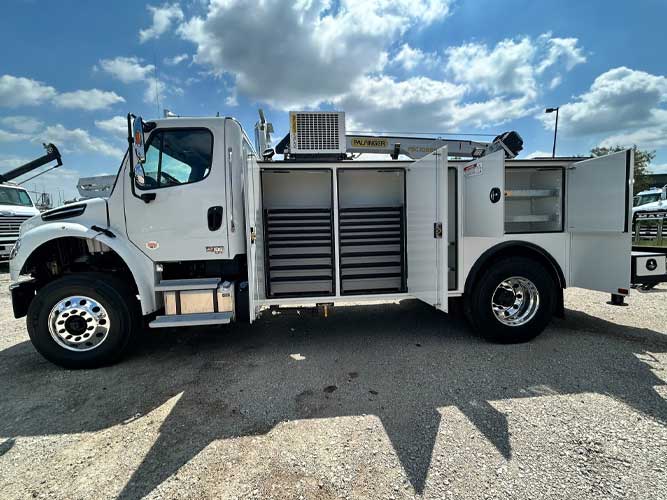 White commercial work truck with open truck body doors showing storage drawers, parked outdoors under partly sunny skies.