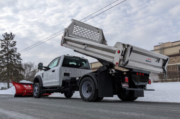 Truck with snow plow and raised dump bed parked on the street in front of a business.